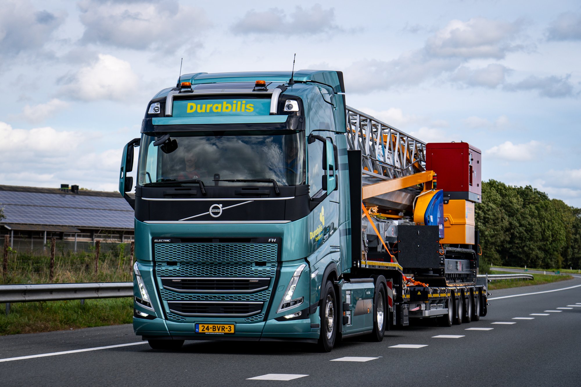 Elektrische vrachtwagen onderweg met bouwmachine snelweg (2)