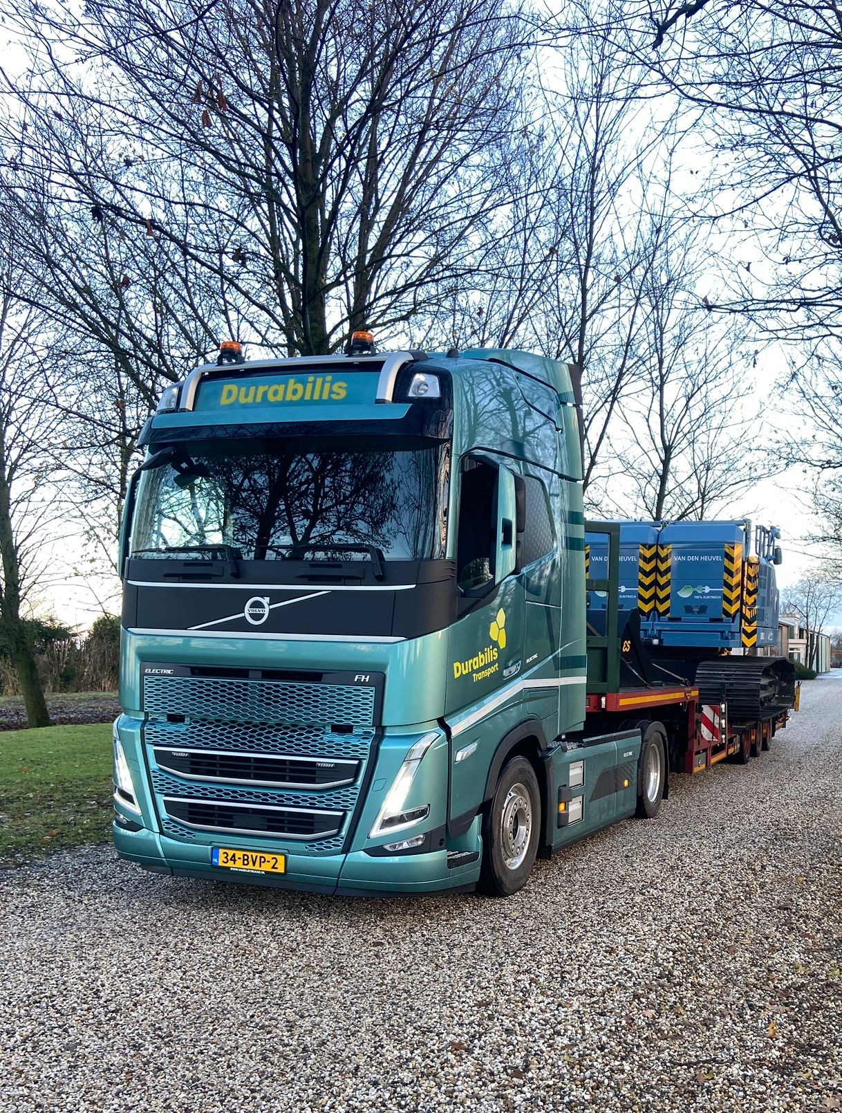 Elektrische vrachtwagen onderweg met bouwmachine grint