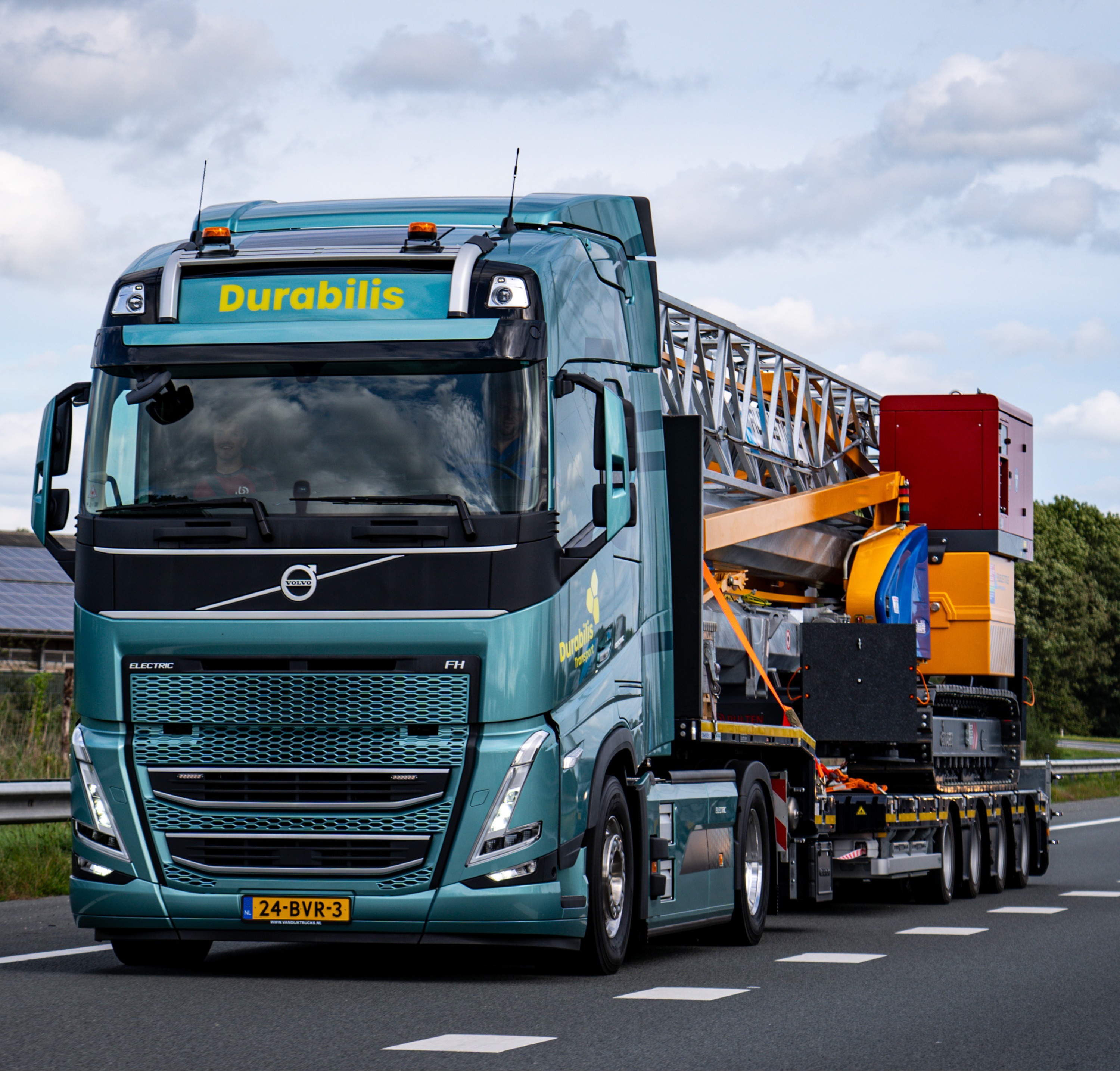 Elektrische vrachtwagen onderweg met bouwmachine snelweg (2)